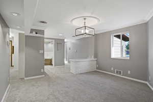 Carpeted empty room featuring ornamental molding and a chandelier