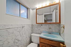 Bathroom featuring tile walls, a textured ceiling, vanity, and toilet