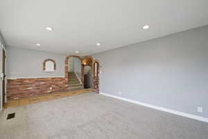 Unfurnished living room featuring a textured ceiling, carpet flooring, and brick wall