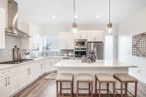 Kitchen with wall chimney exhaust hood, stainless steel appliances, white cabinets, and a center island