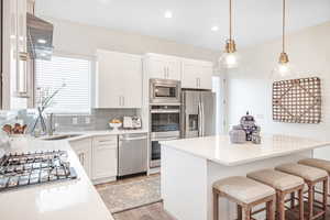 Kitchen featuring tasteful backsplash, sink, white cabinets, hanging light fixtures, and stainless steel appliances