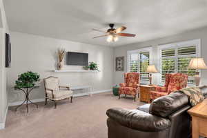 Carpeted living room featuring ceiling fan and a textured ceiling