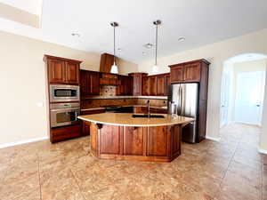 Kitchen with pendant lighting, sink, tasteful backsplash, a center island with sink, and stainless steel appliances