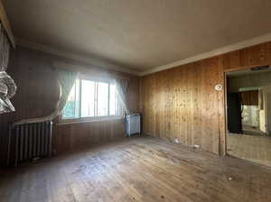 Empty room featuring crown molding, wood walls, radiator heating unit, and hardwood / wood-style flooring