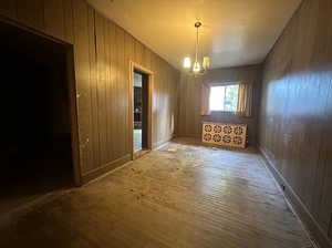 Spare room featuring an inviting chandelier, wooden walls, and hardwood / wood-style floors