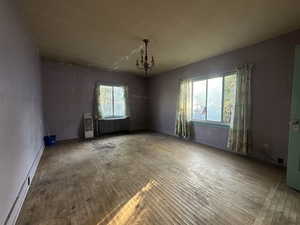 Unfurnished room with radiator, hardwood / wood-style flooring, a notable chandelier, and a healthy amount of sunlight