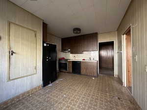 Kitchen featuring wood walls, black appliances, dark brown cabinets, sink, and extractor fan