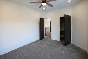 Unfurnished bedroom with dark carpet and ceiling fan