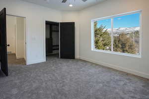 Unfurnished bedroom with dark colored carpet, a mountain view, and ceiling fan