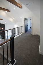 Corridor featuring lofted ceiling with beams and dark carpet