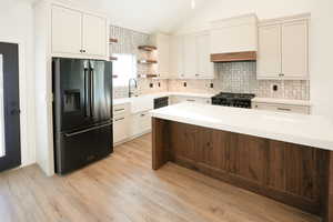 Kitchen featuring lofted ceiling, sink, light hardwood / wood-style flooring, backsplash, and black appliances