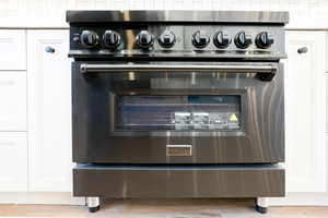 Interior details with white cabinetry, high end stainless steel range, and light hardwood / wood-style floors