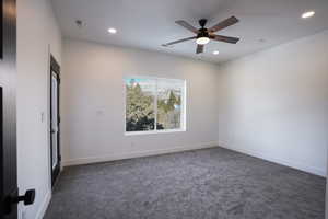 Spare room with ceiling fan and dark colored carpet