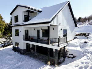 Snow covered back of property with a balcony and a garage