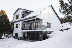 Snow covered rear of property featuring a balcony and a garage