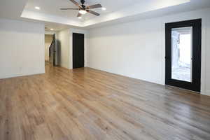 Empty room featuring a tray ceiling, ceiling fan, and light wood-type flooring