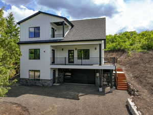 Modern farmhouse with stairs, a balcony, board and batten siding, stone siding, and dirt driveway