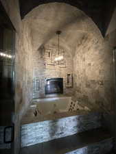 Bathroom featuring an inviting chandelier, lofted ceiling, plus walk in shower, and tile walls