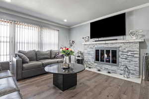 Living room featuring wood-type flooring, a stone fireplace, and crown molding