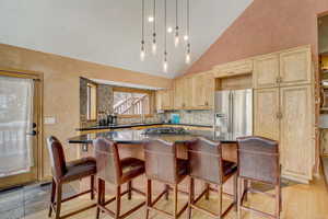 Kitchen featuring stainless steel fridge, high vaulted ceiling, light brown cabinets, decorative light fixtures, and sink