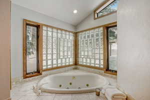 Bathroom featuring a healthy amount of sunlight, vaulted ceiling, and a relaxing tiled tub