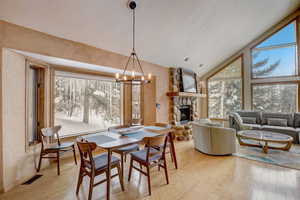 Dining room with high vaulted ceiling, a stone fireplace, a chandelier, and light hardwood / wood-style flooring