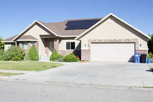 View of front of house with a garage, solar panels, and a front lawn