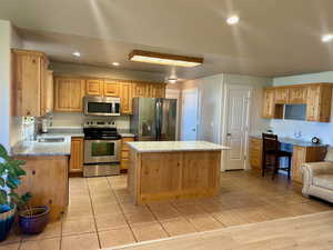 Kitchen featuring light hardwood / wood-style flooring, stainless steel appliances, sink, light stone countertops, and a center island