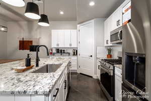 Kitchen with hanging light fixtures, white cabinetry, backsplash, stainless steel appliances, and sink