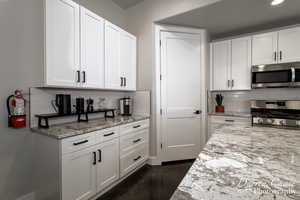 Kitchen featuring backsplash, light stone countertops, stainless steel appliances, and white cabinets