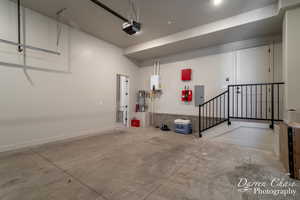 Garage with electric panel, a garage door opener, and tankless water heater