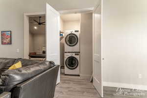 Washroom featuring light hardwood / wood-style floors, stacked washing maching and dryer, and ceiling fan