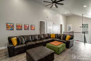 Living room featuring ceiling fan with notable chandelier, light wood-type flooring, a textured ceiling, and high vaulted ceiling