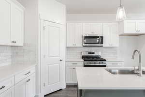 Kitchen featuring sink, appliances with stainless steel finishes, white cabinetry, dark hardwood / wood-style floors, and decorative light fixtures