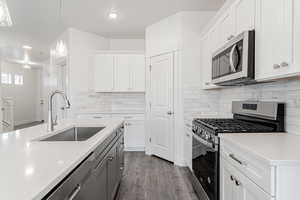 Kitchen with hardwood / wood-style floors, sink, white cabinets, hanging light fixtures, and stainless steel appliances