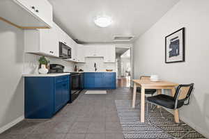 Kitchen with black appliances, blue cabinets, and white cabinetry