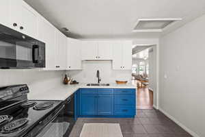 Kitchen featuring blue cabinets, dark tile patterned flooring, sink, white cabinetry, and black appliances