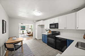 Kitchen with blue cabinets, a textured ceiling, white cabinetry, and black appliances