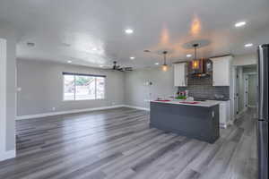 Kitchen with wood-type flooring, white cabinetry, a kitchen island, wall chimney exhaust hood, and decorative light fixtures