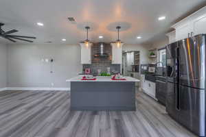 Kitchen with white cabinets, hanging light fixtures, a kitchen island, wall chimney exhaust hood, and appliances with stainless steel finishes