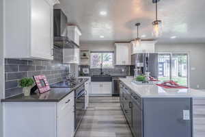 Kitchen featuring pendant lighting, light hardwood / wood-style flooring, wall chimney range hood, white cabinetry, and appliances with stainless steel finishes