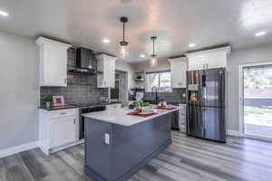 Kitchen with pendant lighting, appliances with stainless steel finishes, wall chimney exhaust hood, and white cabinets