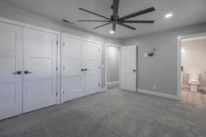 Unfurnished bedroom featuring carpet flooring, ceiling fan, ensuite bathroom, and multiple closets