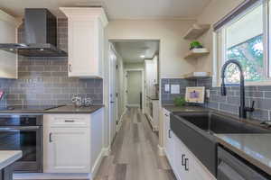 Kitchen featuring white cabinetry, wall chimney range hood, light hardwood / wood-style flooring, stainless steel appliances, and backsplash