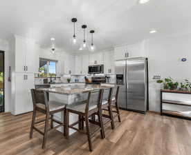 Kitchen featuring hanging light fixtures, white cabinets, a kitchen island, stainless steel appliances, and light hardwood / wood-style flooring