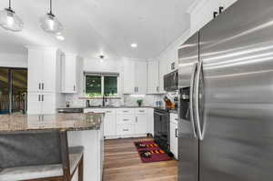 Kitchen with pendant lighting, dark stone counters, dark wood-type flooring, white cabinets, and appliances with stainless steel finishes