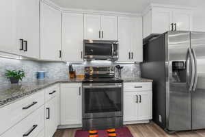 Kitchen featuring wood-type flooring, decorative backsplash, stainless steel appliances, and white cabinets