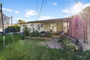 Back of house with central AC, a trampoline, covered porch, and a yard