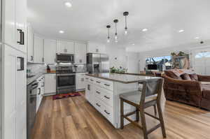 Kitchen featuring light hardwood / wood-style floors, white cabinetry, a breakfast bar, stainless steel appliances, and a center island