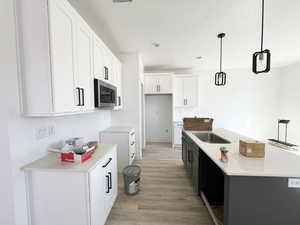 Kitchen featuring pendant lighting, white cabinetry, sink, a kitchen island with sink, and light hardwood / wood-style floors